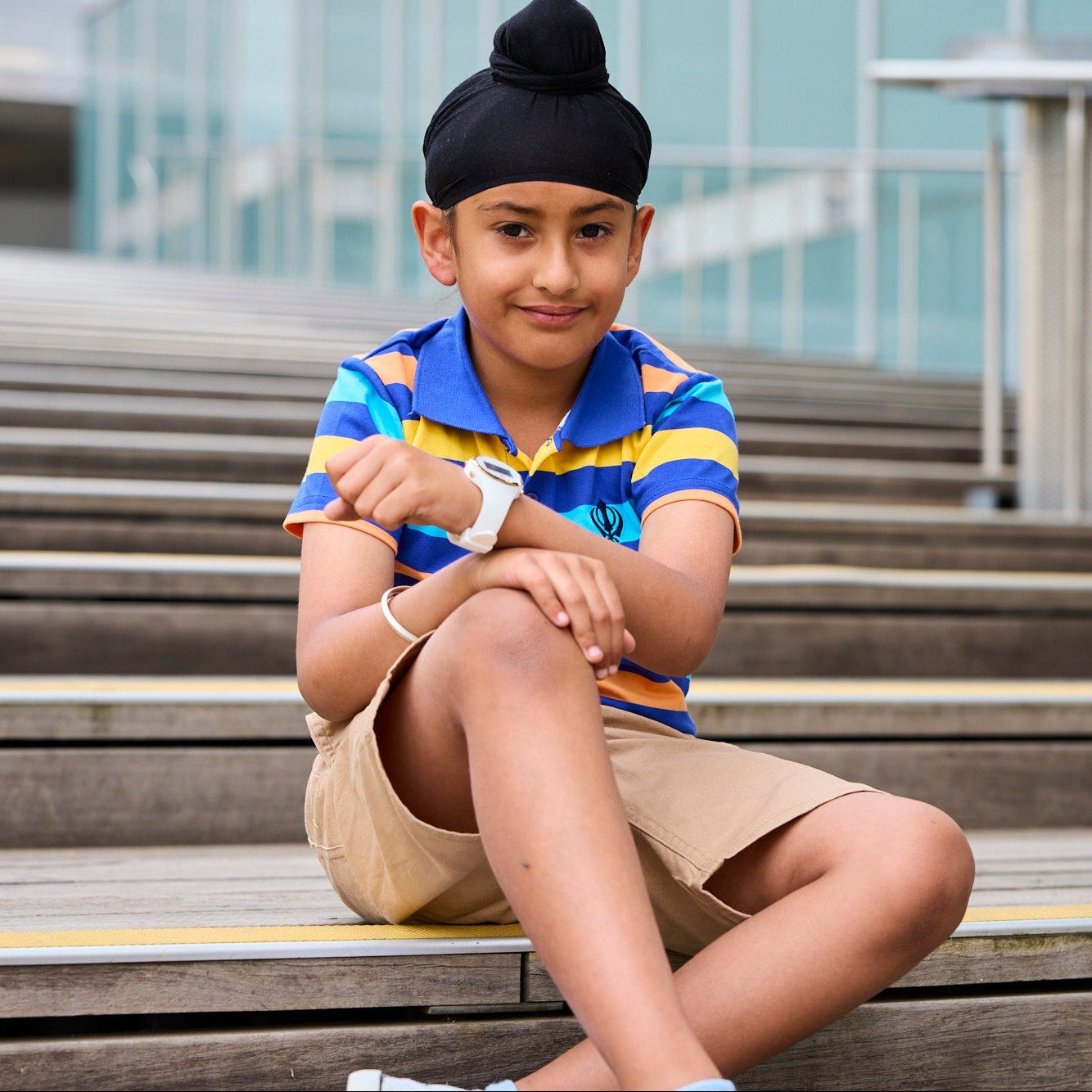 Child sitting on steps wearing a colorful polo shirt and beige shorts.